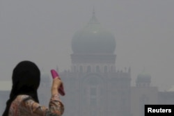 FILE - A woman looks toward the Malaysian prime minister's office in Putrajaya, which is shrouded in haze from fires in Indonesia, Oct. 6, 2015.