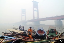 FILE - A woman disembarks from a boat as the Ampera Bridge is shrouded in haze from wildfires in Palembang, South Sumatra, Indonesia, Sept. 29, 2015.