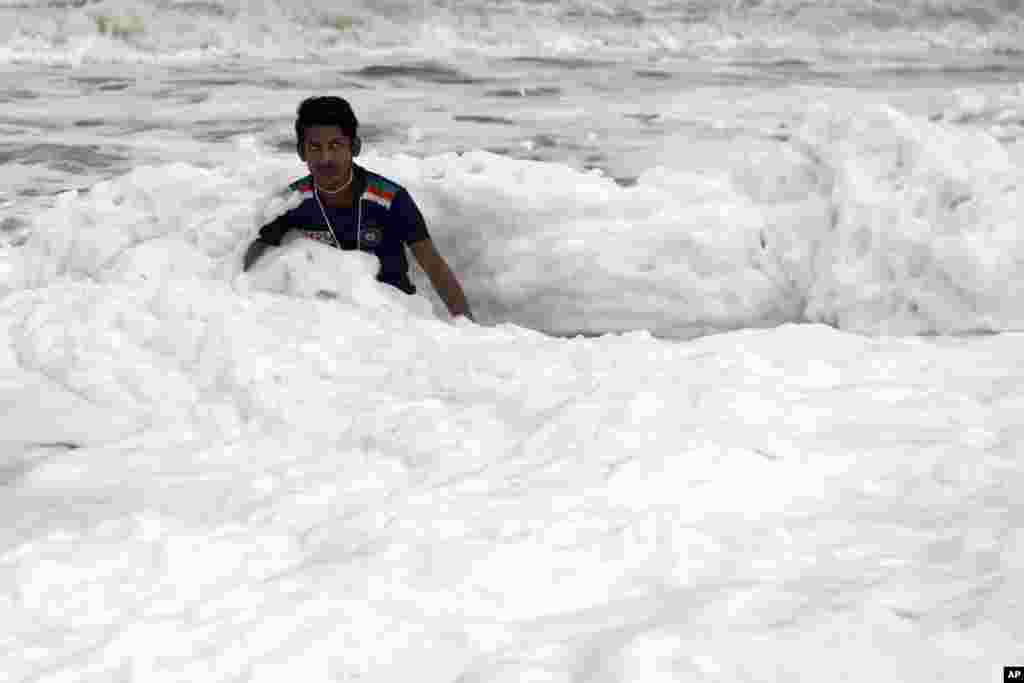 A man plays over foamy discharge caused by pollutants, as it mixes with the surf at Marina beach in Chennai, India.