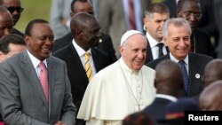 El papa Francisco sonríe mientras camina a la par del presidente keniano, Uhuru Kenyatta (izquierda) a su llegada a Nairobi, Kenia.