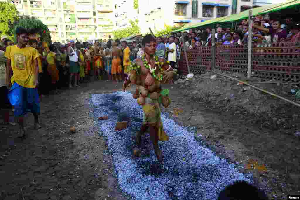 A Hindu devotee with coconuts attached to his body with pins, walks on hot coal during anniversary celebrations of a Hindu temple in Rangoon, Burma.