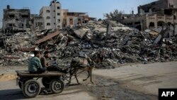 Palestinski muškarci voze se zapregama koje vuku magarci pored zgrada uništenih tokom izraelskih napada u Beit Lahiji u sjevernoj Gazi, 26. februara 2024.