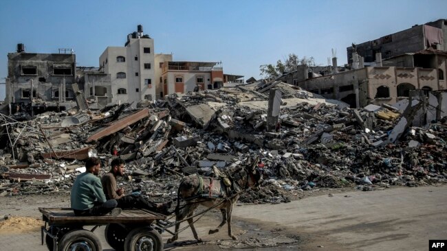26일 가자지구 북부 이스라엘군 공습 잔해 곁에서 팔레스타인인들이 당나귀 수레를 타고 이동하고 있다.