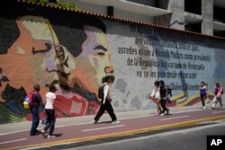 People walk past a mural of late Venezuelan President Hugo Chavez and Venezuelan President Nicolas Maduro in Caracas, Venezuela, on July 27, 2024, the day before voters go to the ballot box in the presidential election.