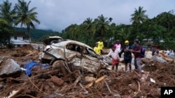 Anggota tim penyelamat berdiri di samping mobil yang rusak akibat tanah longsor pada hari kedua pencarian korban pada 31 Juli 2024, setelah tanah longsor menerjang distrik Wayanad, negara bagian Kerala, India. (Foto: AP/Rafiq Maqbool) 