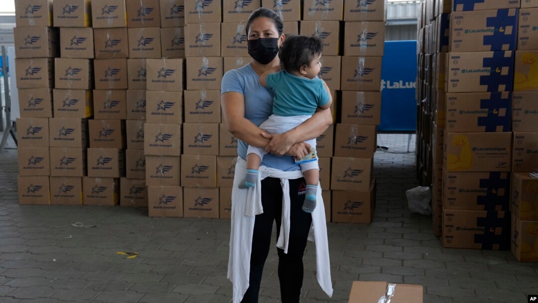ARCHIVO - Una mujer con su hijo en brazos al lado de un kit de alimentos donados por el gobierno municipal después de haber recibido la vacuna contra COVID-19 de Sinovac en Guayaquil, Ecuador, el 22 de julio de 2021. 