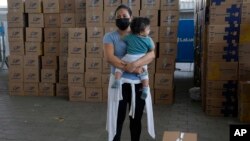 ARCHIVO - Una mujer con su hijo en brazos al lado de un kit de alimentos donados por el gobierno municipal después de haber recibido la vacuna contra COVID-19 de Sinovac en Guayaquil, Ecuador, el 22 de julio de 2021. 