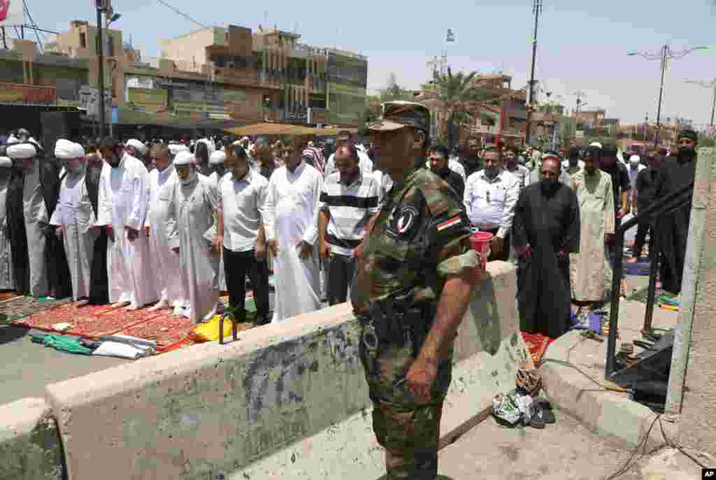 A member of the Iraqi security forces stands next to followers of Shiite cleric Muqtada al-Sadr attending open-air Friday prayers in Sadr City, Baghdad, July 18, 2014.