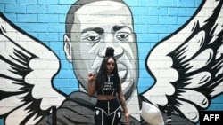 A woman raises her fist in front of a mural of George Floyd in Houston, Texas on June 8, 2020.