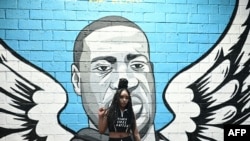 A woman raises her fist in front of a mural of George Floyd in Houston, Texas on June 8, 2020.