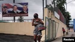 En La Habana, Cuba, el 12 de abril de 2021, una mujer pasa frente a un cartel donde aparecen las figuras del fallecido presidente de los Consejos de Estado y de Ministros, Fidel Castro, su hermano Raúl Castro y el actual presidente Miguel Díz-Canel.