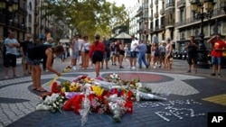 A woman places a flower around a memorial tribute of flowers, messages and candles on Barcelona's historic Las Ramblas in Barcelona, Aug. 16, 2018, the day before to the anniversary of the attacks that took place here on Aug. 17, 2017 killing 16 people and injuring more than 120. 