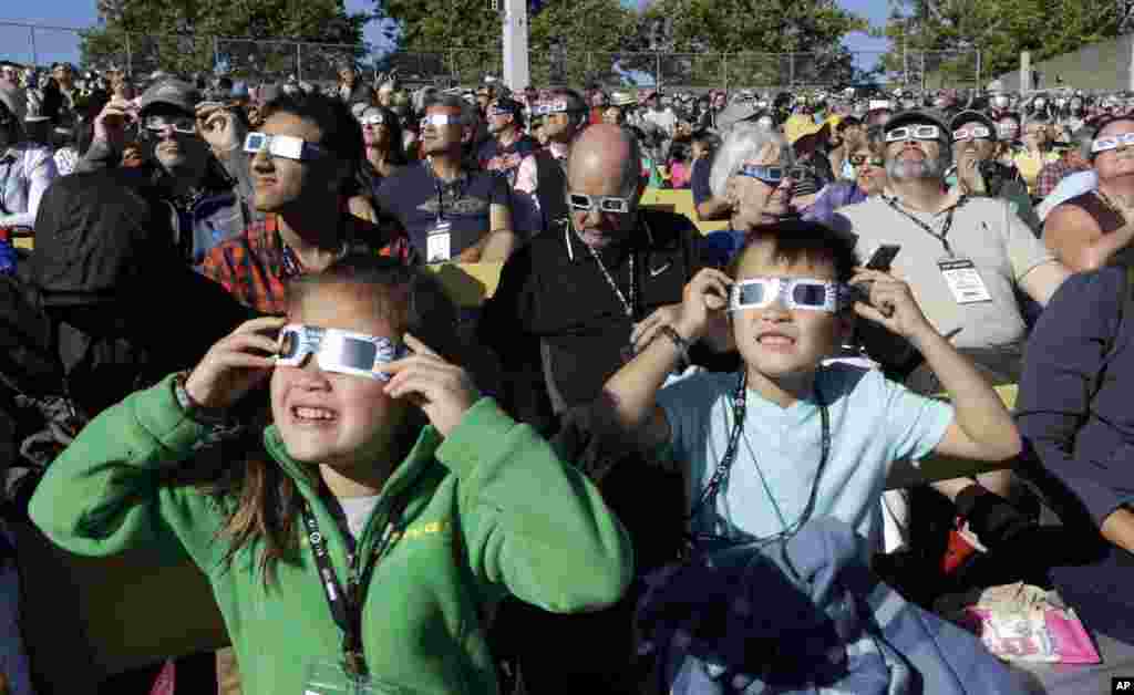 A crowd wears protective glasses as they watch the beginning of the solar eclipse from Salem, Ore., Monday, Aug. 21, 2017.