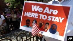 FILE - A protester holds a sign during a "Here to Stay" rally at the Irish Famine Memorial in Boston, July 6, 2017. U.S. lawmakers have introduced legislation to all a path to citizenship for immigrants brought into the U.S. as children.