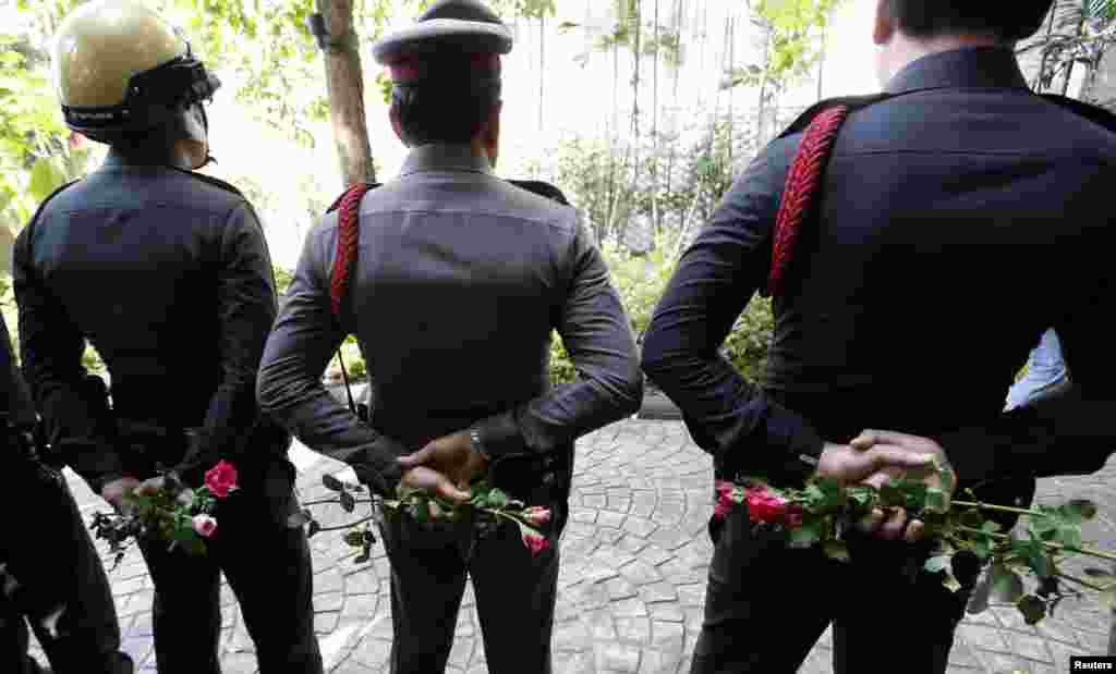 Thai police officers hold roses given by pro-army supporters behind their back as they stand guard outside the Australian embassy in Bangkok, June 4, 2014.