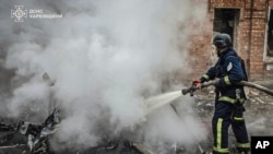 In this photo provided by the Ukrainian Emergency Services on Nov. 25, 2024, a rescue worker puts out a fire of a burned car in the yard of an apartment building damaged by a Russian strike on a residential neighborhood in Kharkiv, Ukraine. 