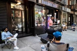 Customers wait on the sidewalk before receiving haircuts while a DJ plays music outside Ace of Cuts barbershop, June 22, 2020, in New York.