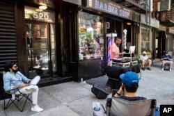 Customers wait on the sidewalk before receiving haircuts while a DJ plays music outside Ace of Cuts barbershop, June 22, 2020, in New York.