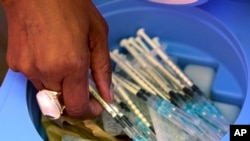 FILE - A health worker picks syringes as seniors get vaccinated with the first dose of the Pfizer coronavirus vaccine at the newly-opened mass vaccination program for the elderly at a drive-thru vaccination center in Johannesburg, South Africa, May 25, 2021.