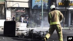 Lính cứu hỏa Iran bên cạnh một chiếc xe máy bị đốt cháy trên đường phố ở trung tâm Tehran, ngày 3/10/2012