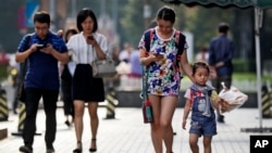 Pedestrians view their smartphones as they walk along a sidewalk in Beijing, Aug. 9, 2017. China has become one of the world's largest mobile phone markets as the phones grow more popular among all age groups in China.