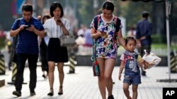 Pedestrians view their smartphones as they walk along a sidewalk in Beijing, Aug. 9, 2017. China has become one of the world's largest mobile phone markets as the phones grow more popular among all age groups in China.