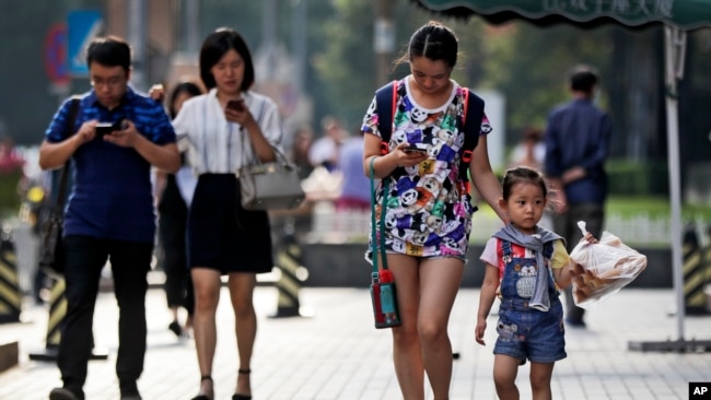 Pedestrians view their smartphones as they walk along a sidewalk in Beijing, Aug. 9, 2017. China has become one of the world's largest mobile phone markets as the devices grow more popular among all age groups in China.