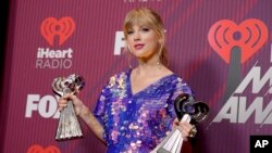 FILE - Taylor Swift poses in the press room with the awards for tour of the year for her "Reputation Stadium Tour" and best music video for "Delicate" at the iHeartRadio Music Awards, March 14, 2019, at the Microsoft Theater in Los Angeles. 