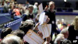 Caucus goers seated in the section for Democratic presidential candidate former Vice President Joe Biden hold up their first votes as they are counted at the Knapp Center on the Drake University campus in Des Moines, Iowa, Feb. 3, 2020.