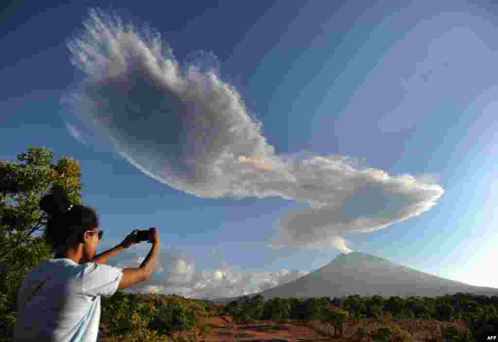 A woman takes photos as Mount Agung volcano sends up another plume of smoke, seen from the Kubu subdistrict in Karangasem Regency on Indonesia&#39;s resort island of Bali, Indonesia.