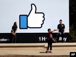 FILE - Visitors take photos in front of the Facebook logo at the company's headquarters, March 28, 2018, in Menlo Park, Calif.