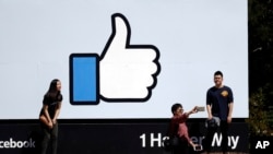 Des visiteurs se faisant photographier devant le logo Facebook au siège social de l'entreprise, le 28 mars 2018, à Menlo Park, en Californie.