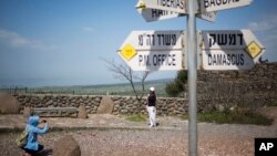 Tourists pose for photograph next to a mock road sign for Damascus, the capital of Syria, and other capitals and cities and a cutout of a soldier, in an old outpost in the Israeli controlled Golan Heights near the border with Syria, March 22, 2019.