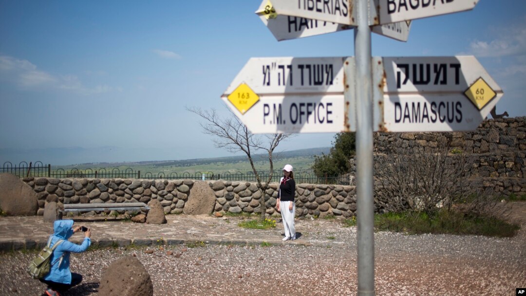 Tourists pose for photograph next to a mock road sign for Damascus, the capital of Syria, and other capitals and cities and a cutout of a soldier, in an old outpost in the Israeli controlled Golan Heights near the border with Syria, March 22, 2019.