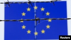 A barbed wire is seen in front of a European Union flag at an immigration reception center in Bicske, Hungary, June 25, 2015. 