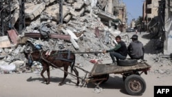Palestinian boys ride a donkey-pulled cart near a building destroyed in Israeli bombardment in Rafah in the southern Gaza Strip on March 31, 2024.