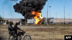 (FILE) Two men ride a motorcycle close to a fire raging in northeastern Syria.