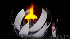 Naomi Osaka stands beside the Olympic flame after lighting it during the opening ceremony in the Olympic Stadium at the 2020 Summer Olympics, Friday, July 23, 2021, in Tokyo, Japan. (AP Photo/David J. Phillip)