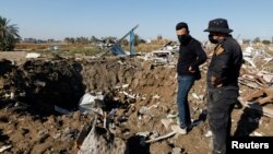 伊拉克真主党旅成员和一名男子在伊拉克的希拉查看美国空袭后的现场。(2023年12月26日)