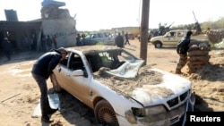 Seorang pria mengamati mobil rusak di dekat pangkalan militer di Barsis, 50 km dari Benghazi, setelah ledakan bom bunuh diri. 