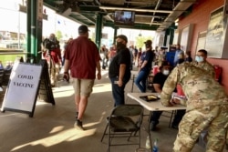 People pass by a temporary vaccination clinic the Washoe County Health District organized with the Nevada National Guard offering COVID-19 shots at the home season opener for the Reno Aces Triple-A minor league baseball team in Reno, May 13, 2021.