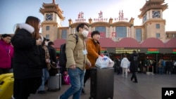 Para wisatawan mengenakan masker saat berjalan keluar dari stasiun kereta api di Beijing, Senin, 20 Januari 2020.