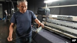 Shigeru Uchida, a weaver at Momotaro Jeans, holds a wooden shuttle next to a vintage loom machine in Kojima, Okayama prefecture, Japan, on Sept. 4, 2024. (AP Photo/Ayaka McGill)