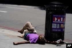 FILE - A homeless person lies on the sidewalk while holding a water bottle, Sunday, July 2, 2023, in downtown Los Angeles. (AP Photo/Damian Dovarganes, File)