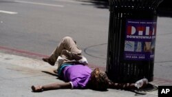 Beskućnik leži na trotoaru držeći flašu vode, u nedjelju, 2. jula 2023., u centru Los Angelesa.