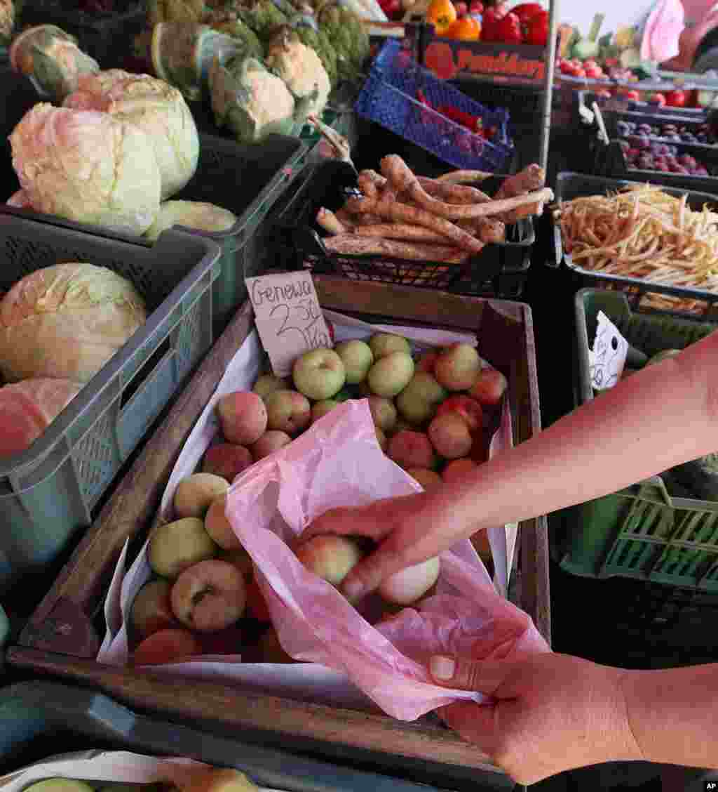 Một phụ nữ bỏ táo mới mua vào túi tại một khu chợ ở Warsaw, Ba Lan. Nga cho biết đã cấm hầu hết trái cây và rau quả nhập khẩu từ Ba Lan. Nhiều người tin rằng lệnh cấm được áp dụng như một sự trả đũa vì Ba Lan ủng hộ lệnh trừng phạt của EU đối với Nga trong cuộc xung đột vũ trang ở Ukraine.