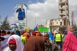 FILE - Somalis walk past a billboard showing candidate Omar Abdulkadir Ahmedfiqi in Mogadishu, Jan. 29, 2021.