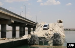 FILE - Members of the Syrian Democratic Forces (SDF) alliance stand guard next to a bridge that was destroyed by the Islamic State (IS) group after they took control of the river crossing and rebuilt the bridge as US-backed Kurdish and Arab fighters advance into the Islamic State (IS) jihadist's group bastion of Manbij, in northern Syria, on June 23, 2016.