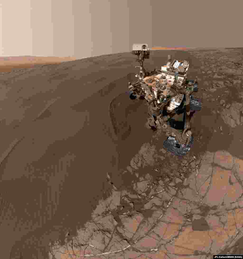 Foto robot penjelajah Mars milik NASA, Curiosity, menunjukkan robot tersebut di &quot;Namib Dune,&quot; tempat robot tersebut beraktivitas termasuk menggoresi bukit pasir dengan rodanya dan mengambil sampel pasir untuk dianalisa di laboratorium.