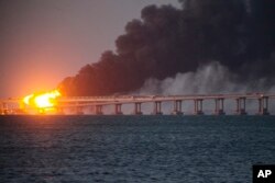 Api dan asap membubung dari Jembatan Krimea yang menghubungkan daratan Rusia dan semenanjung Krimea di atas Selat Kerch, di Kerch, Krimea, Sabtu, 8 Oktober 2022. (Foto: AP)